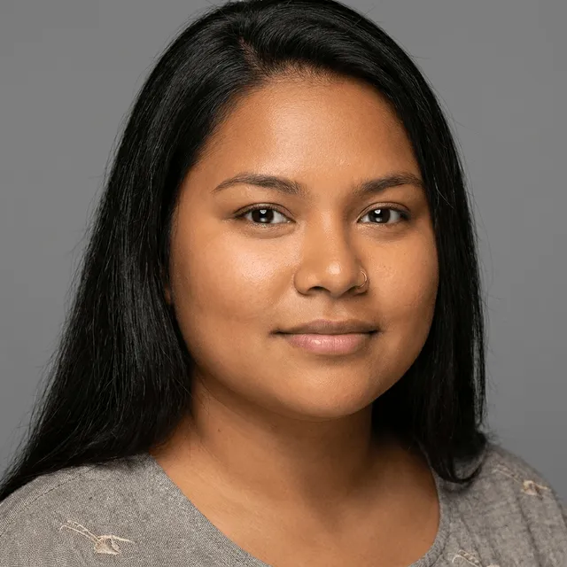 Young woman with long straight dark hair and a small nose ring, wearing a gray textured top, with a slight smile.