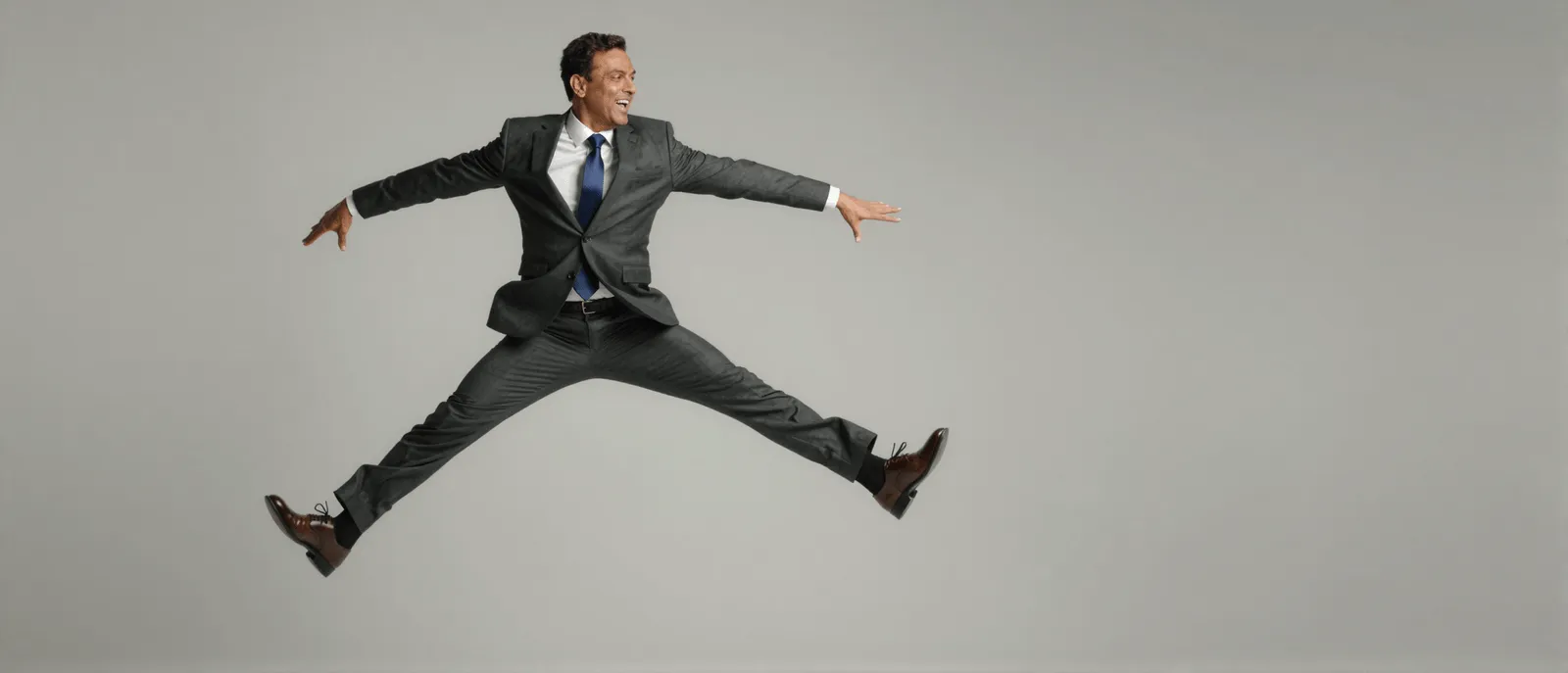 A businessman in a suit jumping joyfully against a plain grey backdrop