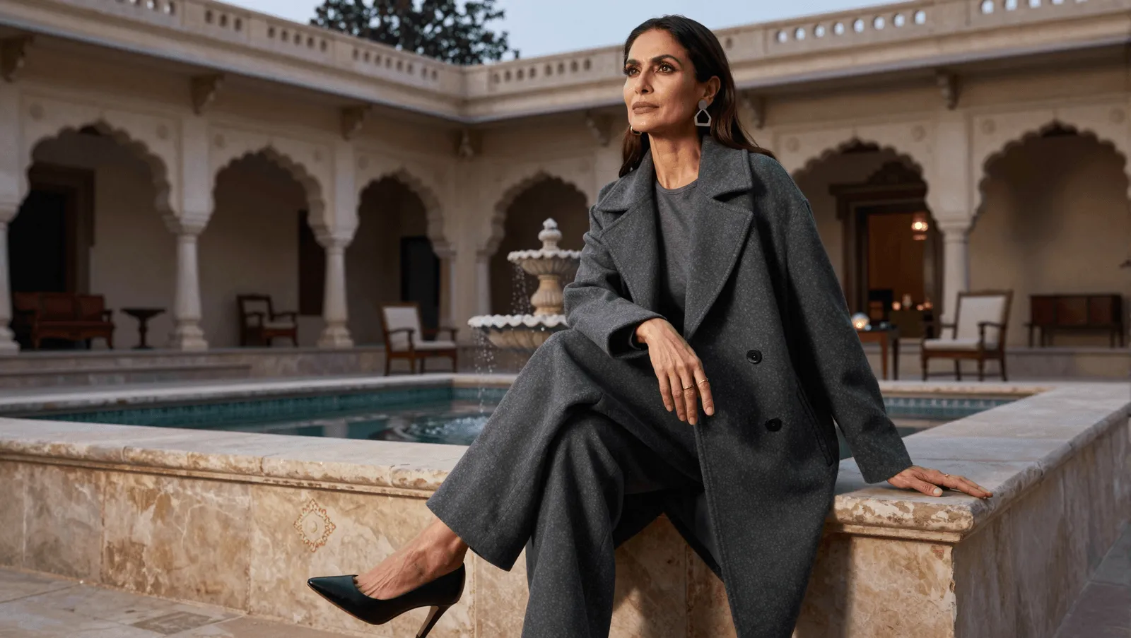An elegant woman seated poolside in a heritage courtyard at dusk