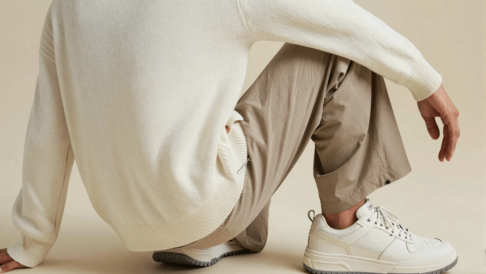 Close-up detail of a cream sweater, beige trousers, and white sneakers